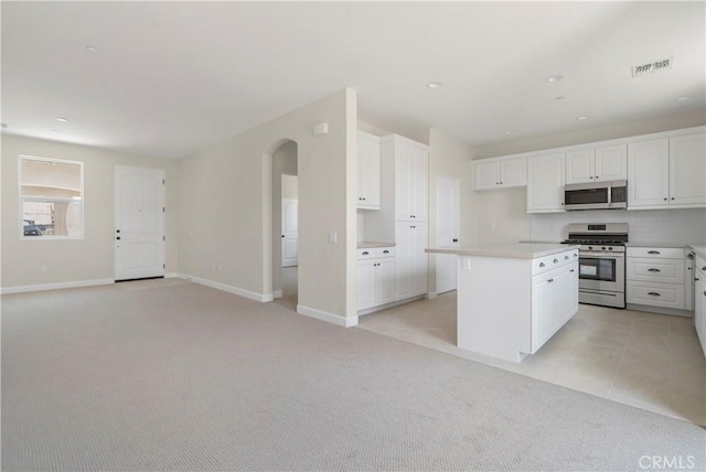 kitchen with light colored carpet, white cabinetry, appliances with stainless steel finishes, and a kitchen island