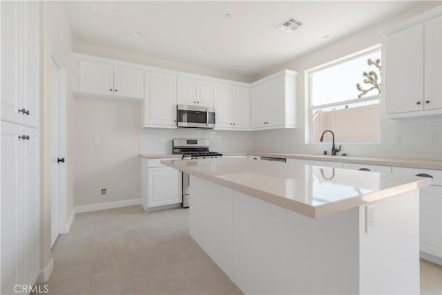 kitchen featuring white cabinets, appliances with stainless steel finishes, light tile patterned floors, and a kitchen island