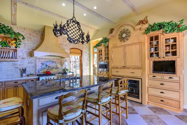 kitchen with premium range hood, dark stone counters, a breakfast bar, a center island with sink, and stainless steel microwave