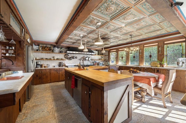 kitchen featuring dishwasher, backsplash, a kitchen island with sink, decorative light fixtures, and butcher block counters