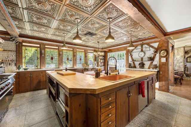 kitchen featuring a healthy amount of sunlight, sink, butcher block counters, and an island with sink