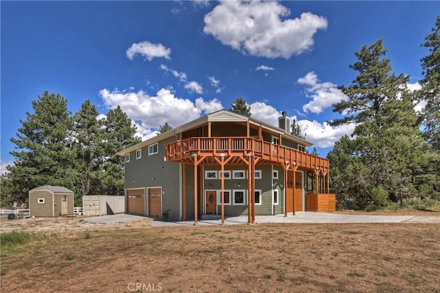 rear view of property with a storage shed, a patio, a garage, and a deck