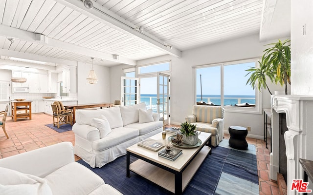 tiled living room featuring beamed ceiling, a wealth of natural light, and a water view