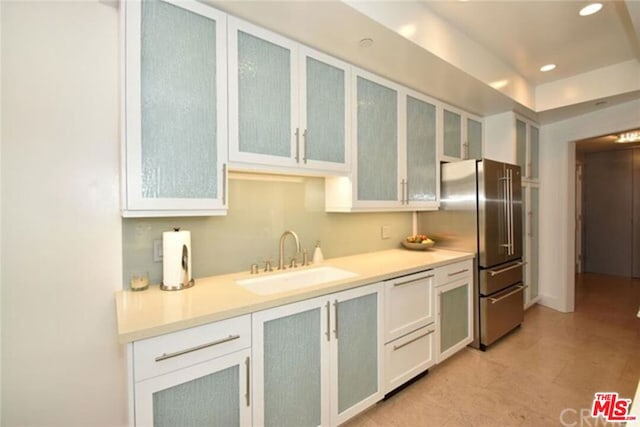 kitchen featuring white cabinetry, a tray ceiling, stainless steel fridge, sink, and light tile floors