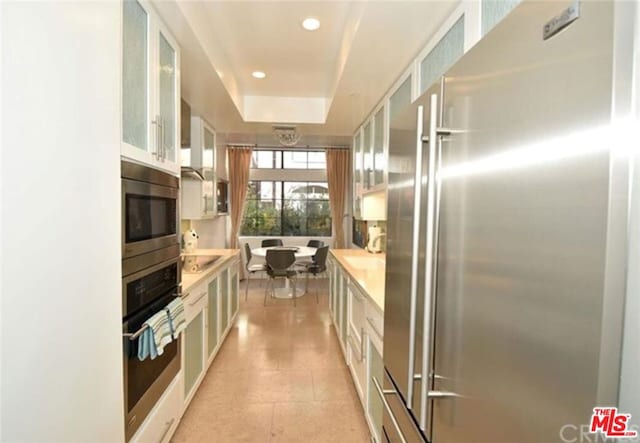 kitchen featuring light tile floors, white cabinetry, a tray ceiling, and black appliances