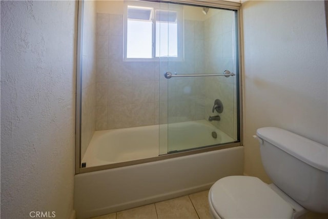 bathroom featuring tile patterned flooring, toilet, and bath / shower combo with glass door