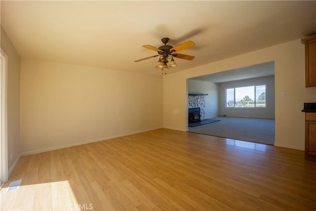 unfurnished living room featuring ceiling fan, light wood-type flooring, and a wood stove