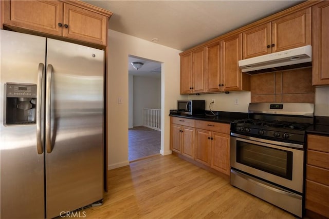 kitchen featuring backsplash, dark stone countertops, light wood-type flooring, and appliances with stainless steel finishes