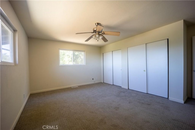 unfurnished bedroom featuring two closets, dark carpet, and ceiling fan