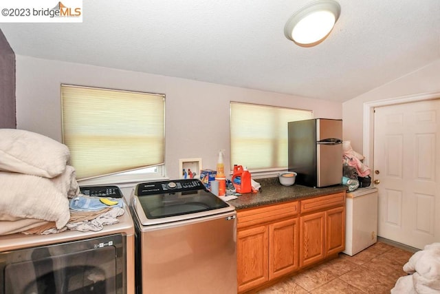 kitchen with light tile flooring, washing machine and dryer, vaulted ceiling, and stainless steel refrigerator