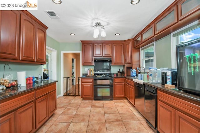 kitchen with sink, light tile floors, dark stone countertops, black appliances, and a notable chandelier