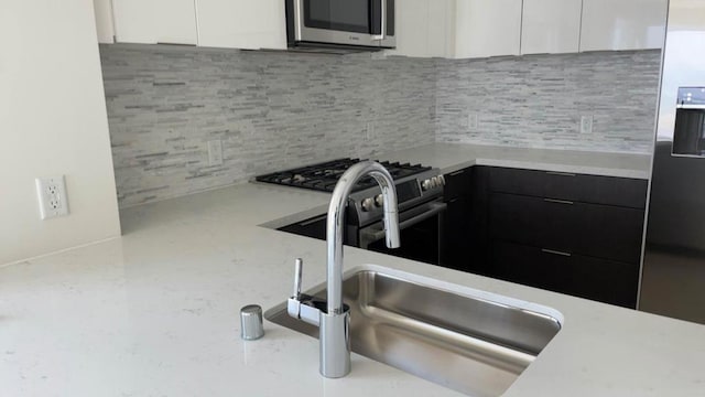 kitchen with tasteful backsplash, sink, white cabinets, and stainless steel appliances