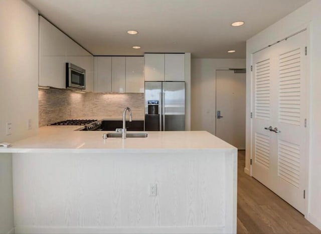 kitchen with white cabinetry, sink, stainless steel appliances, kitchen peninsula, and light wood-type flooring