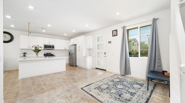 kitchen with white cabinets, appliances with stainless steel finishes, light tile floors, and a center island