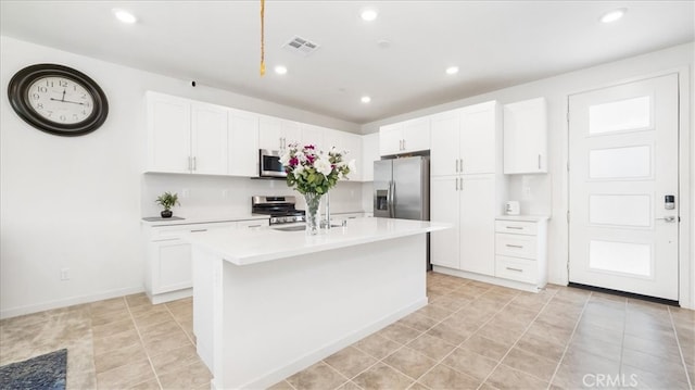 kitchen with appliances with stainless steel finishes, an island with sink, light tile flooring, and white cabinetry