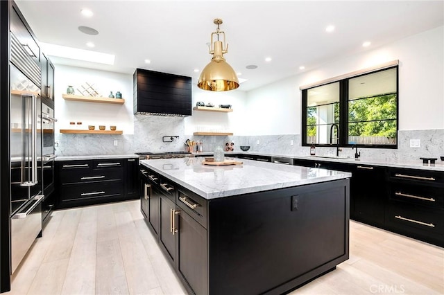 kitchen with light stone countertops, light wood-type flooring, sink, a kitchen island, and hanging light fixtures