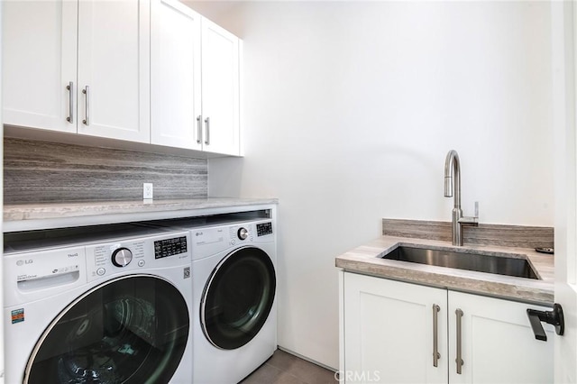 clothes washing area with washing machine and dryer, sink, dark tile patterned floors, and cabinets