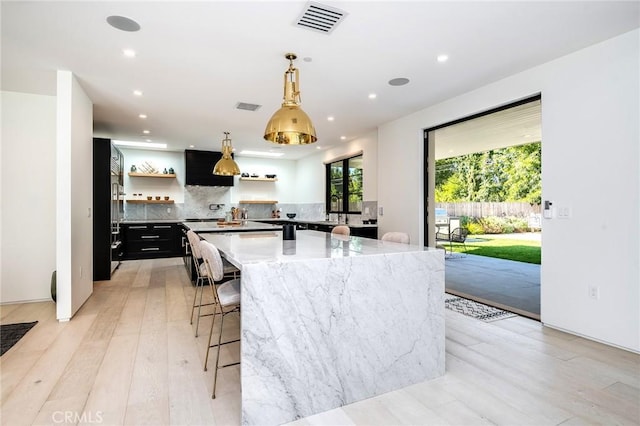 kitchen featuring backsplash, a center island, decorative light fixtures, and light hardwood / wood-style flooring