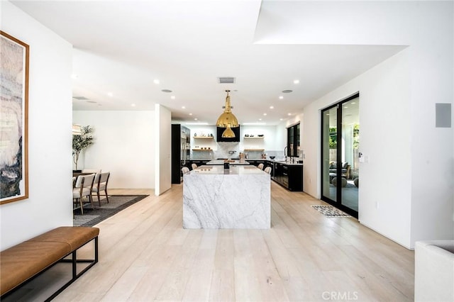 kitchen with light stone countertops, a center island with sink, light hardwood / wood-style floors, and decorative light fixtures