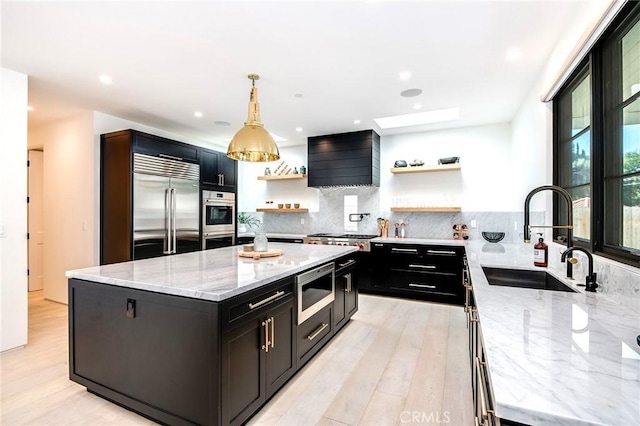 kitchen with a skylight, light stone counters, wall chimney exhaust hood, built in appliances, and a center island