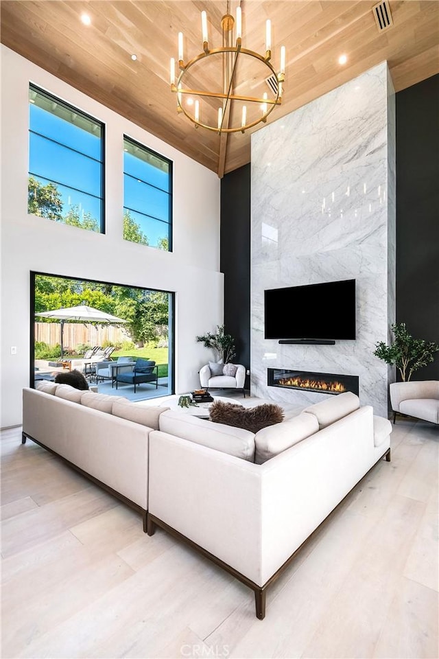 living room with a notable chandelier, wood ceiling, a towering ceiling, and a premium fireplace