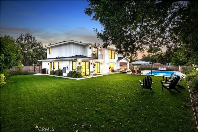 back house at dusk featuring a fenced in pool, central AC, and a yard