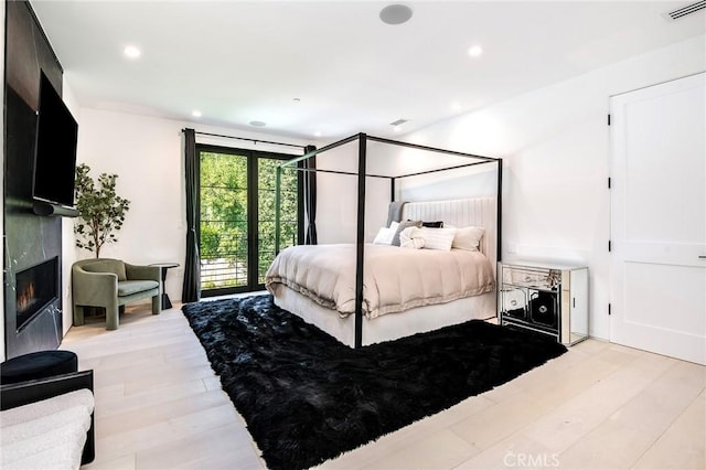 bedroom with access to outside, a premium fireplace, and light wood-type flooring