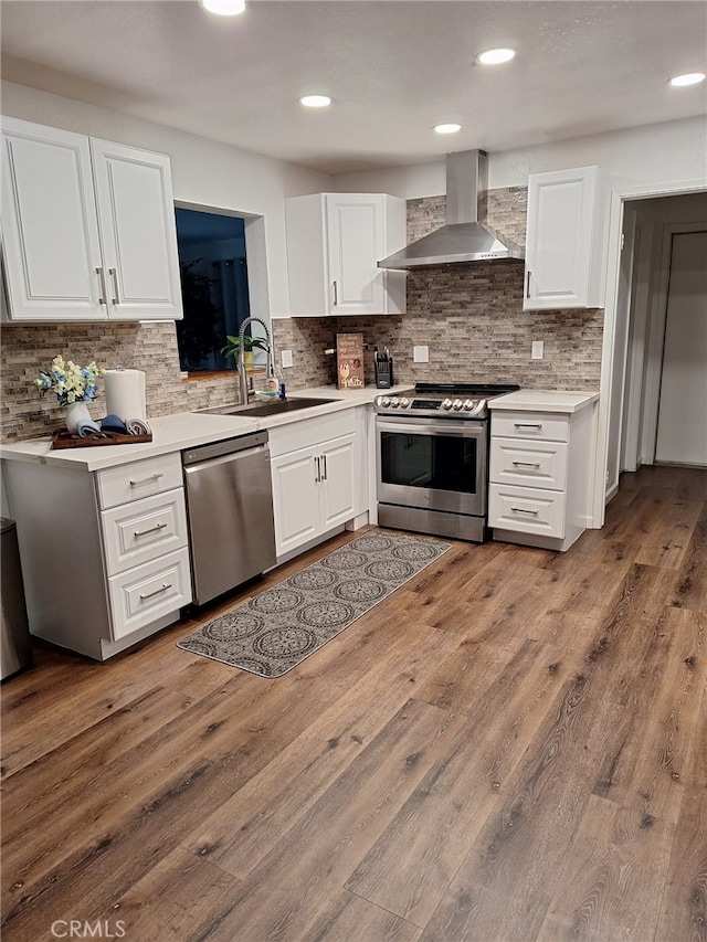 kitchen featuring wall chimney range hood, sink, white cabinetry, stainless steel appliances, and light wood-type flooring