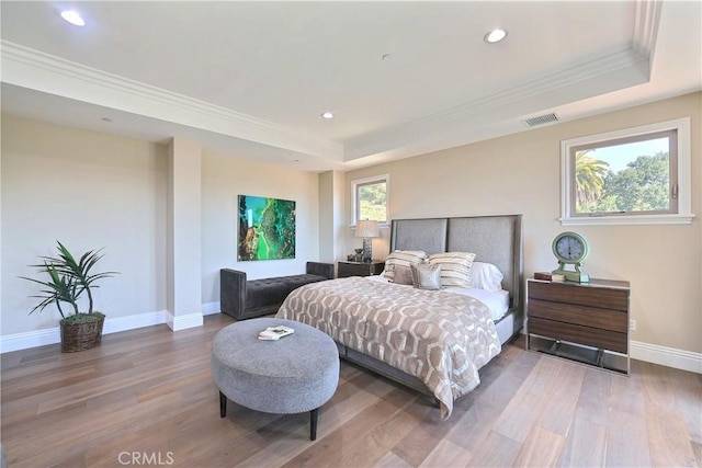 bedroom with hardwood / wood-style floors, a raised ceiling, multiple windows, and ornamental molding