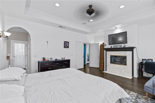 bedroom with ceiling fan, a fireplace, dark wood-type flooring, and a tray ceiling