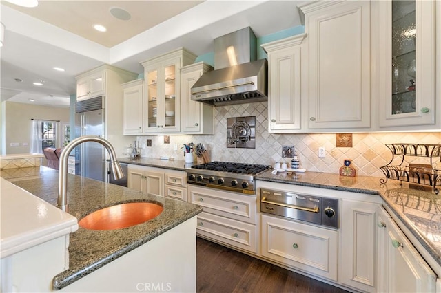 kitchen with white cabinets, wall chimney range hood, sink, dark stone countertops, and stainless steel appliances