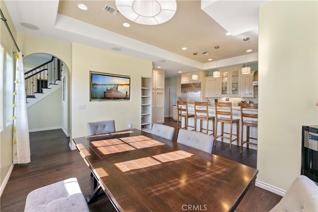 dining room with a tray ceiling, built in shelves, and dark wood-type flooring