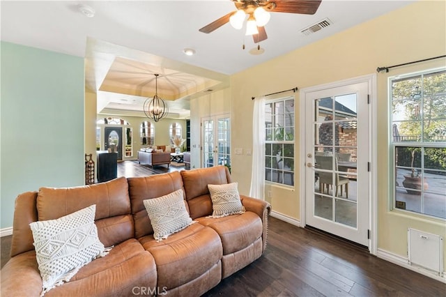 living room featuring ceiling fan with notable chandelier, a raised ceiling, dark wood-type flooring, and french doors