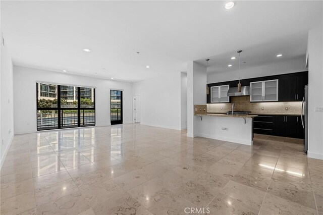 kitchen featuring sink, wall chimney exhaust hood, tasteful backsplash, stainless steel fridge, and a kitchen bar