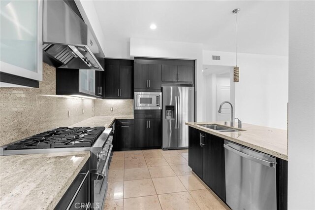 kitchen featuring pendant lighting, wall chimney range hood, sink, appliances with stainless steel finishes, and tasteful backsplash