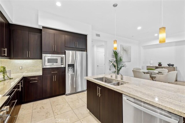 kitchen with light stone countertops, appliances with stainless steel finishes, backsplash, sink, and hanging light fixtures