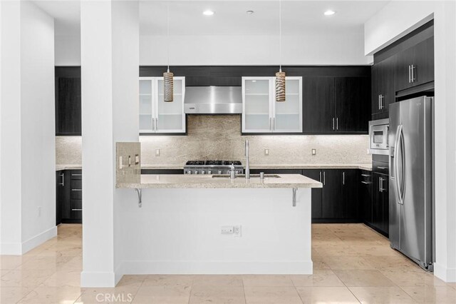 kitchen featuring wall chimney exhaust hood, a kitchen breakfast bar, decorative light fixtures, decorative backsplash, and appliances with stainless steel finishes