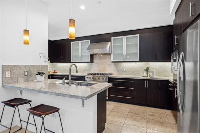 kitchen with kitchen peninsula, appliances with stainless steel finishes, wall chimney exhaust hood, sink, and a breakfast bar area