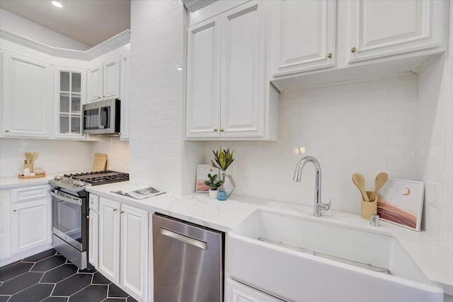 kitchen with white cabinetry, stainless steel appliances, decorative backsplash, sink, and light stone counters