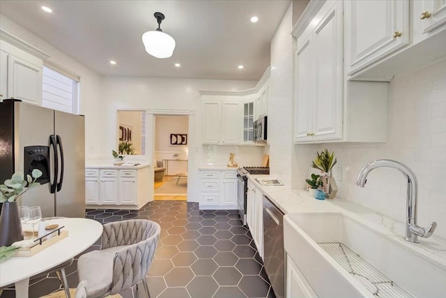 kitchen featuring appliances with stainless steel finishes, backsplash, white cabinets, light stone counters, and sink