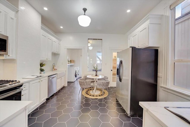 kitchen with washing machine and dryer, appliances with stainless steel finishes, white cabinets, and light stone countertops