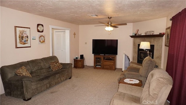 living room featuring ceiling fan, a textured ceiling, carpet, and a tiled fireplace