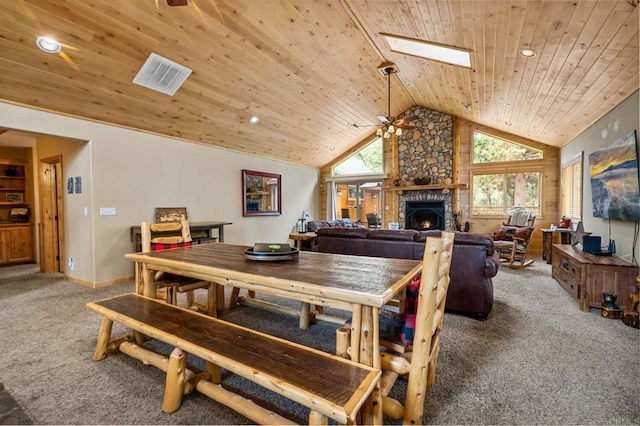 dining space with ceiling fan, a skylight, carpet, a stone fireplace, and wood ceiling