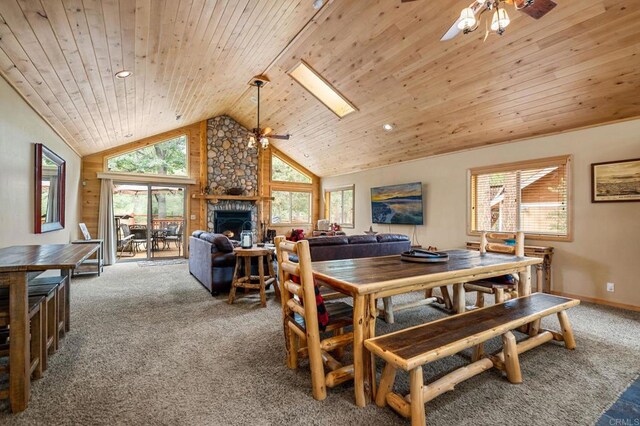 carpeted dining room featuring wood ceiling, a stone fireplace, ceiling fan, and a skylight