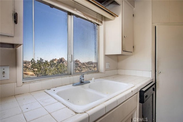 kitchen featuring white cabinetry, sink, stainless steel dishwasher, tile countertops, and light tile patterned floors