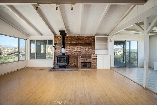 unfurnished living room with hardwood / wood-style flooring, vaulted ceiling with beams, a wood stove, and a textured ceiling