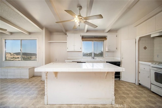 kitchen with electric stove, beam ceiling, tile countertops, black dishwasher, and a kitchen island