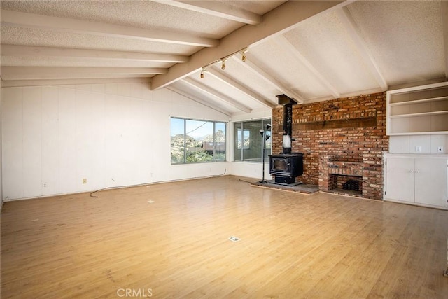 unfurnished living room with hardwood / wood-style floors, vaulted ceiling with beams, a textured ceiling, and a wood stove