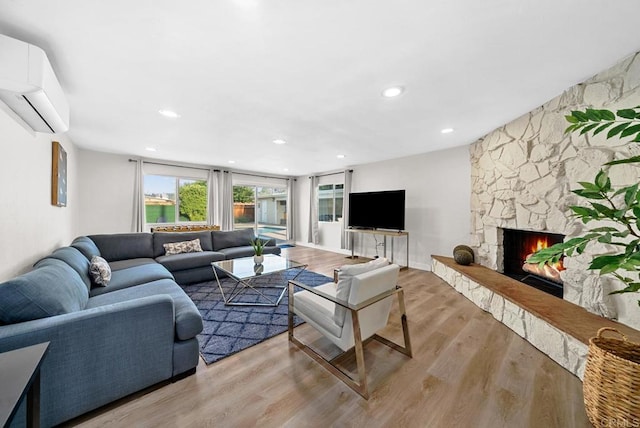 living room with a fireplace, a wall mounted air conditioner, and light wood-type flooring