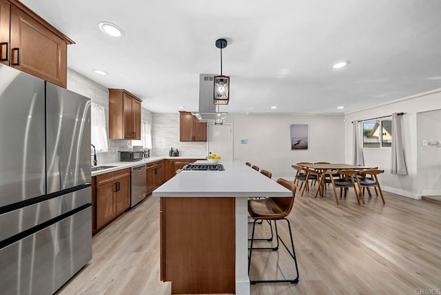 kitchen with hanging light fixtures, light hardwood / wood-style flooring, backsplash, stainless steel appliances, and a center island